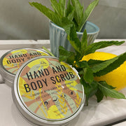 Two tins of Cosy Cottage hand and body scrub  alongside fresh peppermint leaves