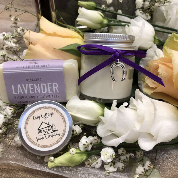 relaxing lavender travel soap, soy wax candle and lip balm bundle on a bed of flowers