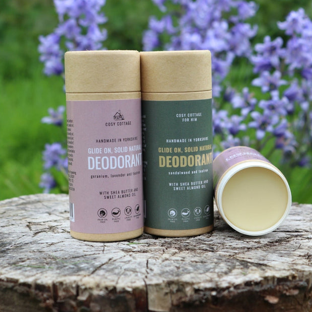 two cosy cottage natural deodorant sticks on a wooden log with blue flowers in the background