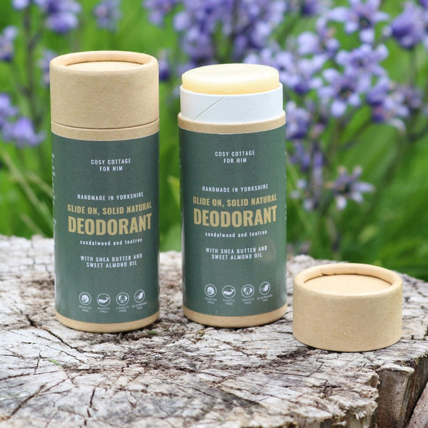 two cosy cottage natural deodorant sticks on a wooden log with blue flowers in the background