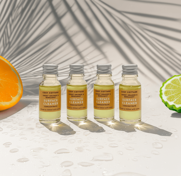 Four bottles of Cozy Cottage Sweet Orange & bergamot biodegradable Surface Cleaner on a light background with an orange and lime slice.