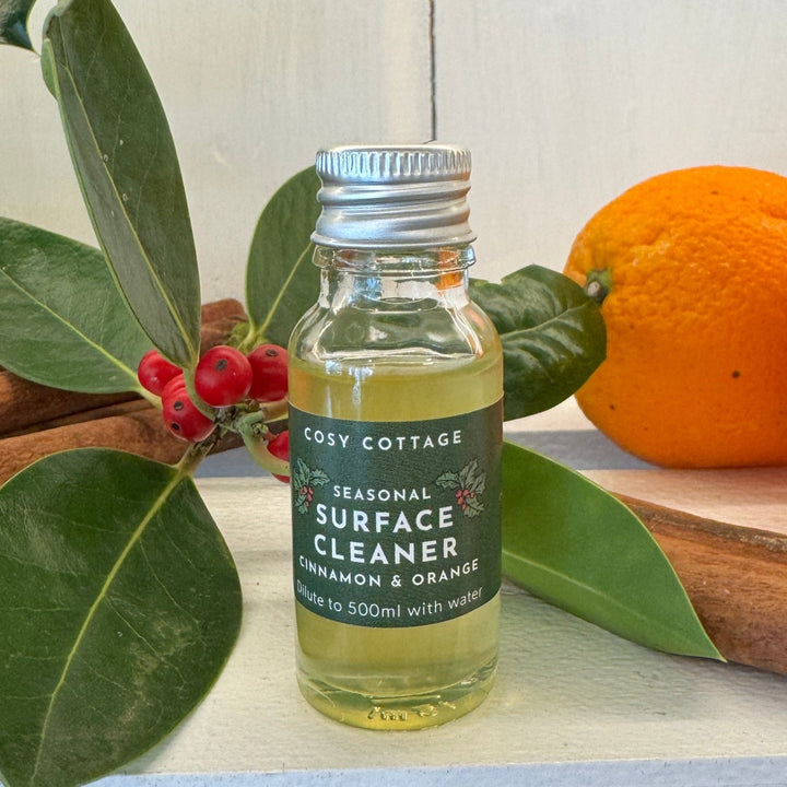 Bottle of natural cleaner with oranges, cinnamon sticks, and green leaves on a wooden surface.