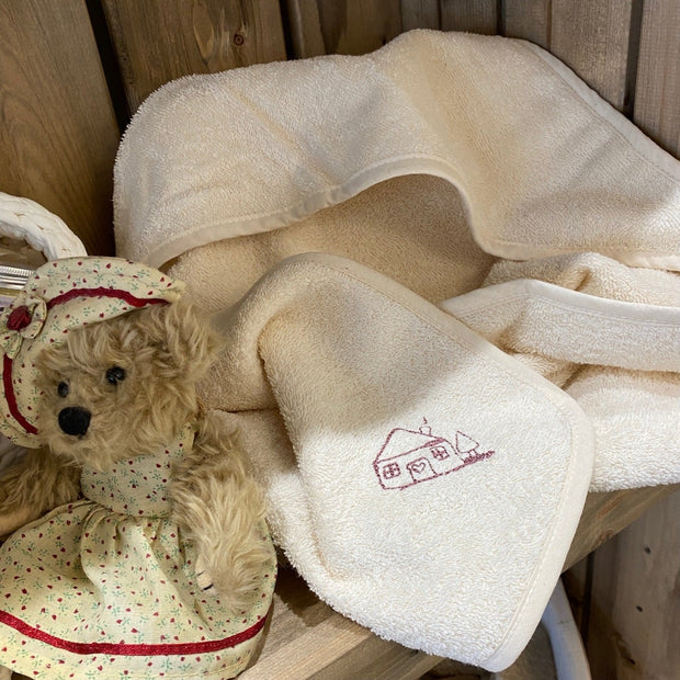 Hooded baby towel next to teddy bear on wooden shelf
