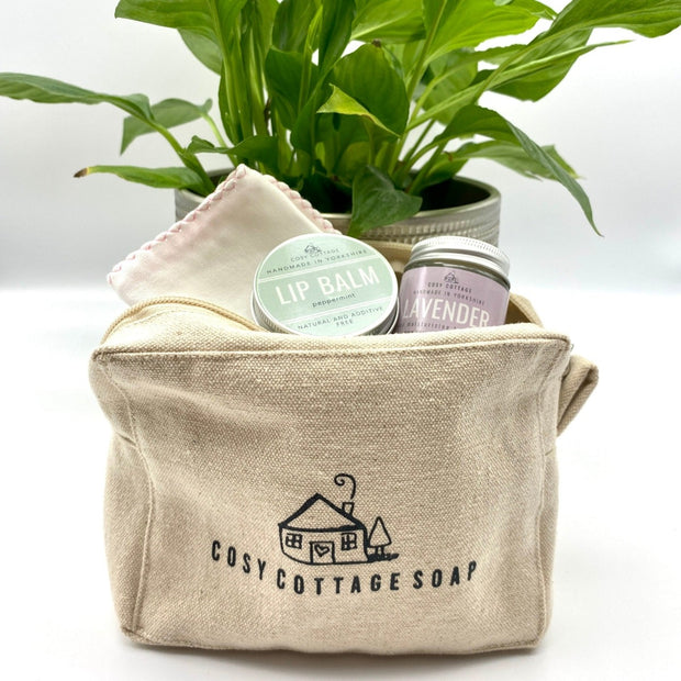 unbleached cosy cottage zip toiletry bag with plant in the background and lip balm and lavender hand cream on the top