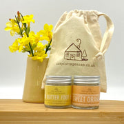 Mango and lemon foot balm and sweet orange hand and body cream in 30ml glass jars with cotton drawstring bag and a vase of yellow flowers