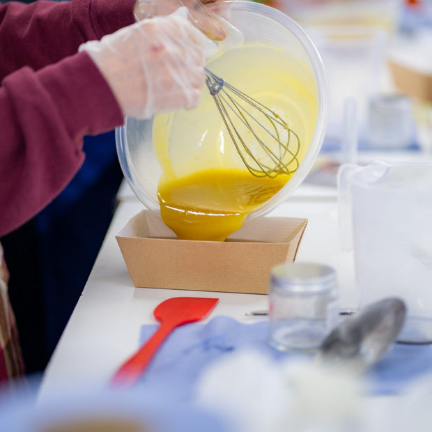 person pouring soap mix into a mould with a whisk