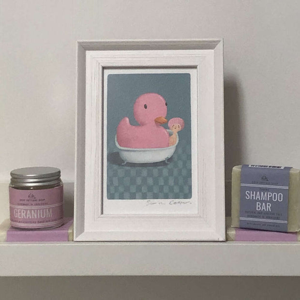 cooperillo framed picture of an oversized pink rubber duck in a bath next to a shampoo bar on a shelf