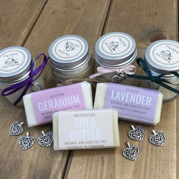 fragranced travel soaps and soy candles arranged on a wooden bench top  with metal charms