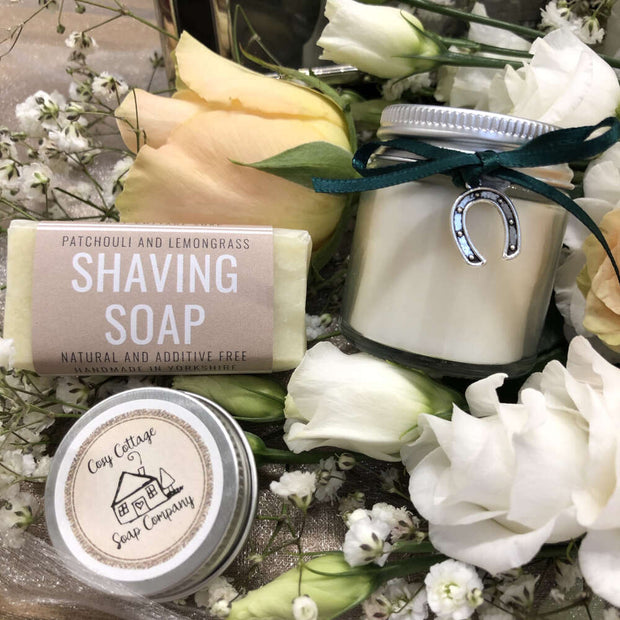 handmade shaving travel soap with soy wax candle and lip balm on a bed of flowers